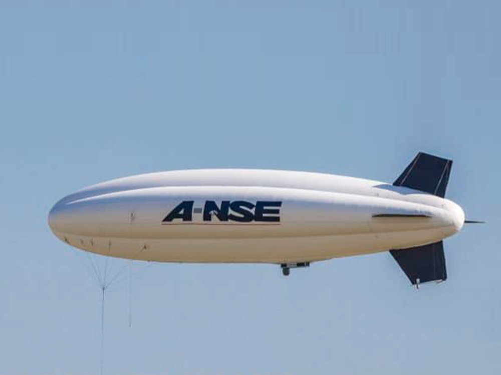 Un dirigeable blanc, une merveille de conception, avec « A-NSE » écrit sur le côté, plane gracieusement dans un ciel bleu clair. Limbus Studio