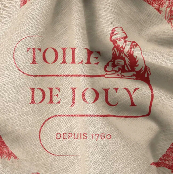 Tissu beige avec impression rouge indiquant "Toile de Jouy" et "Depuis 1760", avec un personnage dessinant au-dessus du texte. Parfait pour les amoureux de la tradition textile française et les fans du Musée de la Toile de Jouy. Limbus Studio