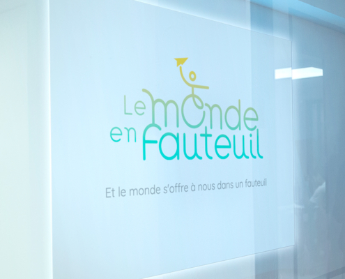 Un panneau lumineux indique "Le monde en fauteuil" avec un graphique en fauteuil roulant, un texte en français en dessous et le hashtag #lemondeenfauteuil - votre destination pour découvrir le fauteuil en ligne. Limbus Studio