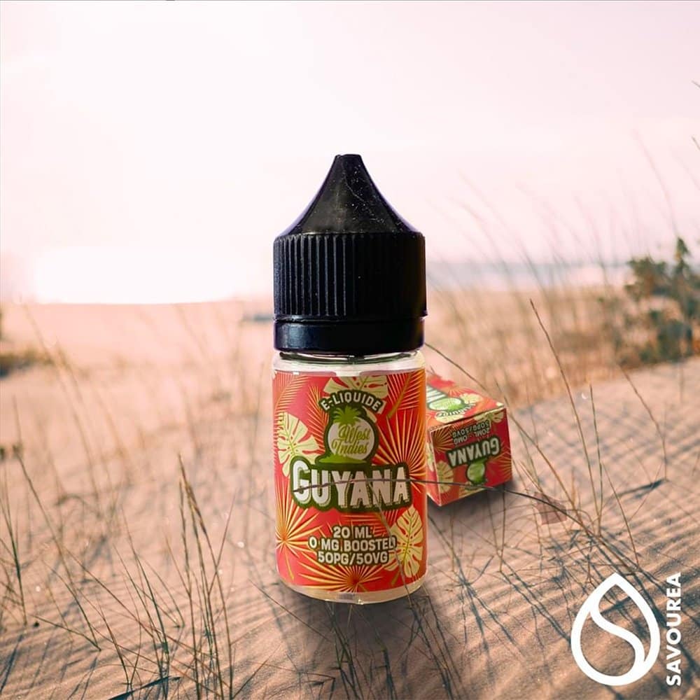 Une bouteille d'e-liquide Guyana avec un emballage tropical se dresse sur le sable, évoquant la touche artistique d'un studio, sur fond de plage flou. Limbus Studio