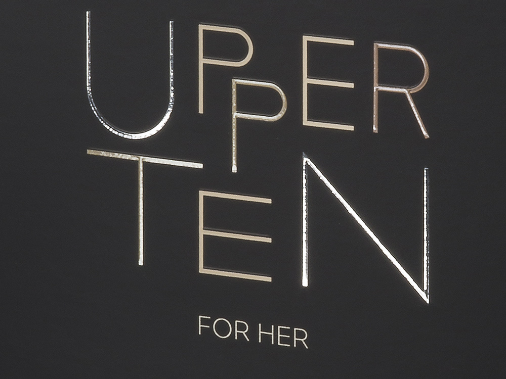 Le texte sur fond sombre indique « UPPER TEN FOR HER » en lettres métalliques, présentant un design exquis.