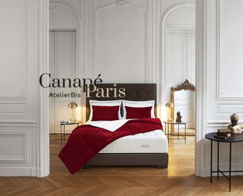 Chambre studio élégante avec murs blancs, parquet et literie rouge mettant en valeur un design raffiné. L'éclairage décoratif ajoute une touche de sophistication. Texte : "Canapé Paris AtelierBis via WordPress. Limbus Studio