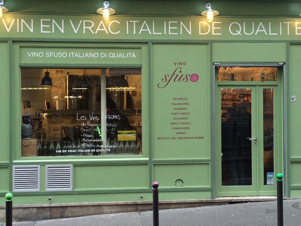 La devanture de ce magasin de vins italien présente une façade verte, rappelant une agence élégante, avec des listes de vins soigneusement présentées sur la vitrine. Limbus Studio