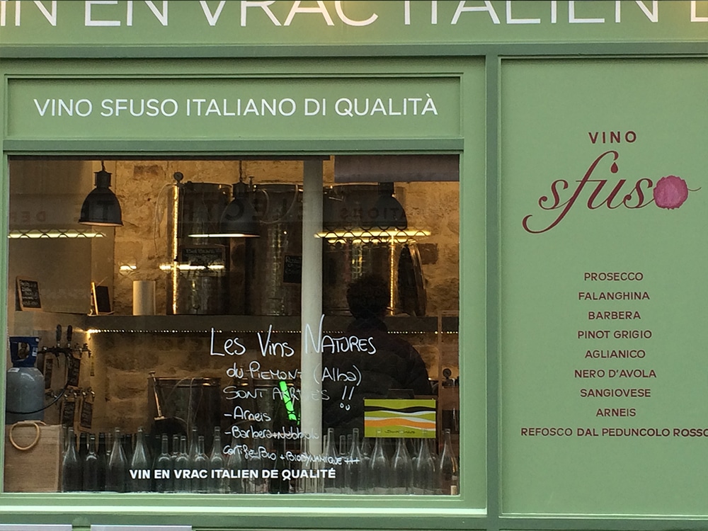 La devanture d'un magasin de vins présente une élégante signalétique verte, rehaussée d'un graphisme impeccable, et une carte des vins manuscrite sur la vitrine. Limbus Studio